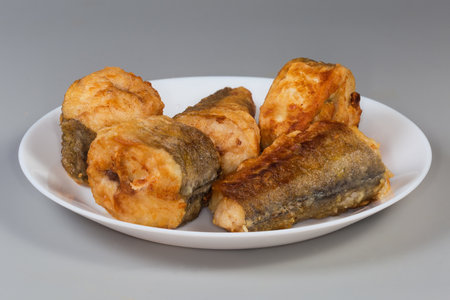 Fried pieces of hake hubbsi, or Argentine hake on white dish on a gray background, side view close-upの写真素材