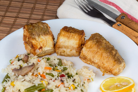 Serving of the pieces of fried Argentine hake, or hake hubbsi with garnish of the boiled mix of rice and vegetables on dish, fragment close-upの写真素材