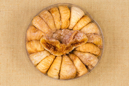 Dried whole figs and one halved fruit atop in the small round plastic packaging on a textile napkin, top viewの写真素材
