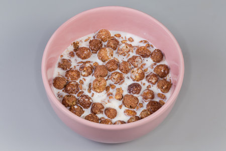 Breakfast cereals in form of mixture of crunchy oat flakes and baked glazed corn balls with cocoa powder drenched in milk in bowl on a gray backgroundの写真素材
