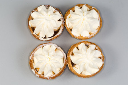 Small tarts, so-called tartlets made with baked shortcrust pastry molds, caramelized pear filling and custard on top on a gray background, top viewの写真素材