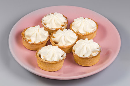 Small tarts, so-called tartlets made with baked shortcrust pastry molds, caramelized pear filling and custard on top on pink dish on a gray backgroundの写真素材