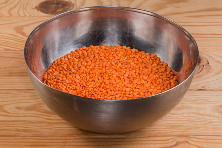 Raw whole red lentil in the stainless steel kitchen bowl on a rustic tableの写真素材