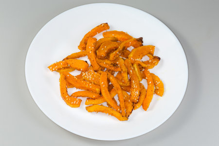 Baked slices of the butternut squash sprinkled with sesame on a white dish on a gray backgroundの写真素材