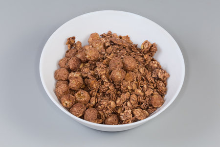 Dry breakfast cereals in form of mixture of crunchy oat flakes and baked glazed corn balls with cocoa powder in bowl on a gray backgroundの写真素材