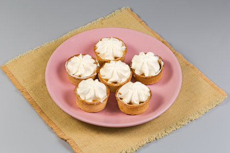 Small tarts, so-called tartlets made with baked shortcrust pastry molds, caramelized pear filling and custard on top on pink dish on a napkin on a gray backgroundの写真素材