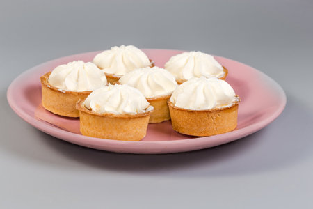 Small tarts, so-called tartlets made with baked shortcrust pastry molds, caramelized pear filling and custard on top on pink dish on a gray background, side view in selective focusの写真素材