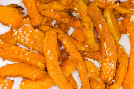 Baked slices of the butternut squash sprinkled with sesame on a white dish, fragment top view close-upの写真素材
