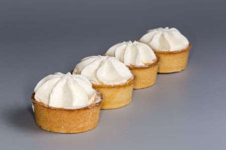Small tarts, so-called tartlets made with baked shortcrust pastry molds, caramelized pear filling and custard on top on a gray background, close-up in selective focusの写真素材