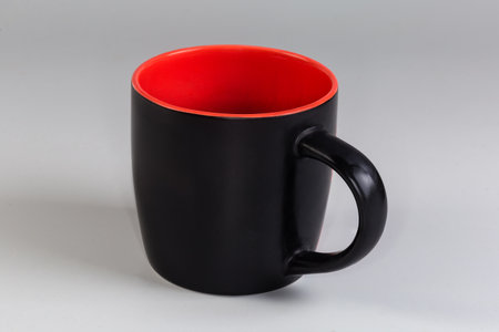 Empty ceramic cup black outside and red inside with handle, side view on a gray backgroundの写真素材