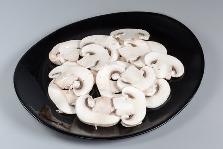 Thin slices of the fresh raw button mushrooms on a black dish on a gray backgroundの写真素材