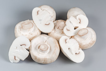 Small heap of whole and sliced fresh raw button mushrooms on a gray surface close-upの写真素材