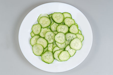Fresh green cucumbers cut into thin circles on a dish, top view on a gray backgroundの写真素材