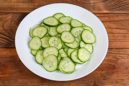 Fresh green cucumbers cut into thin circles on a dish on a rustic tableの写真素材