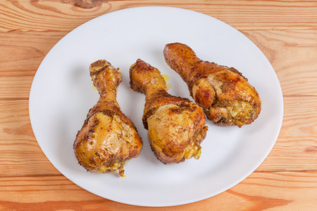 Baked chicken drumsticks with different spices on a white dish on a rustic tableの写真素材