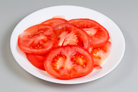 Round slices of the fresh red tomato on a dish on a gray background, side viewの写真素材