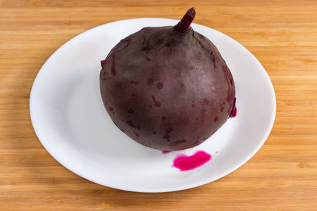 Whole cooked unpeeled young red beetroot round shape in their skin on the white dish on a wooden surfaceの写真素材