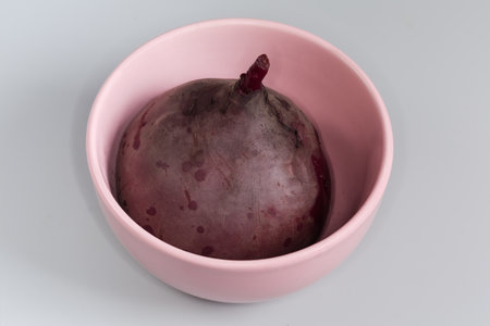 Whole cooked unpeeled young red beetroot round shape in their skin in the pink bowl on a gray backgroundの写真素材