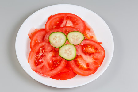 Slices of the fresh red tomato and green cucumber slices atop on a dish on a gray backgroundの写真素材