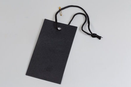 Sale clothing swing tag in the form of the blank black cardton sheet on a black rope with small clasp-pin on a gray backgroundの写真素材
