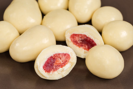 Several whole and two halves of the confections in the form of dried strawberries covered with white chocolate on the brown dish, close-up in selective focusの写真素材