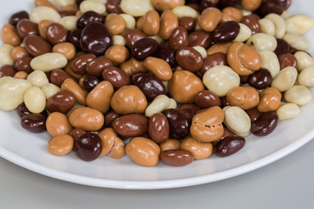 Confections in the form of raisins covered with dark, white and milk chocolate on the white dish on a gray background, fragment close-up in selective focusの写真素材