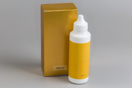 Closed plastic yellow bottle of liquid pharmaceutical product against its cardboard box package with indicating volume on a gray backgroundの写真素材