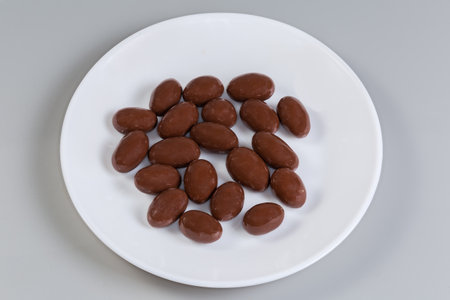 Confections in the form of almond nuts covered with milk chocolate on the white dish on a gray backgroundの写真素材