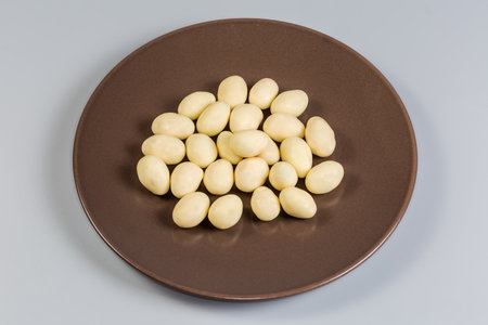 Confections in the form of almond nuts covered with white chocolate on the brown dish on a gray backgroundの写真素材