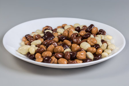 Confections in the form of raisins covered with dark, white and milk chocolate on the white dish on a gray background, side view in selective focusの写真素材