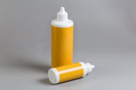 Two closed plastic yellow bottles of different volumes of liquid pharmaceutical product on a gray backgroundの写真素材