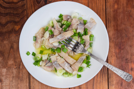 Slice of pickled Atlantic herring impaled on a fork and the same sliced herring with chopped green...