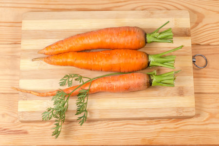 Three washed fresh young carrots with parts of stems on a cutting board on a rustic table, top viewの写真素材