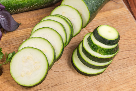 Green zucchini sliced into circles on the wooden cutting board, close-upの写真素材