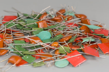 Heap of various ceramic disc and rectangular fixed capacitors and film capacitors with axial and radial connecting leads, side view close-up in selective focus on a gray surfaceの写真素材