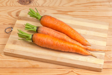 Three washed fresh young carrots with parts of stems on a cutting board on a rustic tableの写真素材