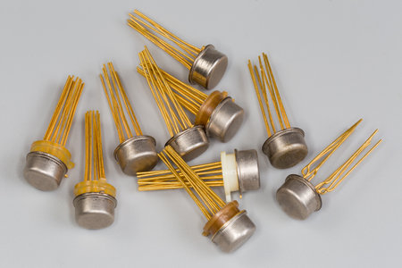 Analog integrated circuits in the round metal packages with gilt pins for thru-hole mount on a printed circuit board close-up on a gray surfaceの写真素材