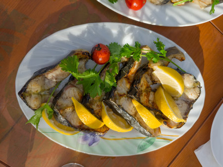 Grilled steaks of the fresh Siberian sturgeon with lemon slices and cilantro twigs on the plate on a table, top viewの写真素材