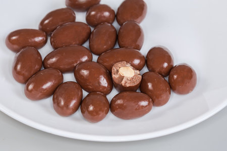 Several whole and one half of the confections in the form of almond nuts covered with milk chocolate on the white dish on a gray background, fragment close-upの写真素材
