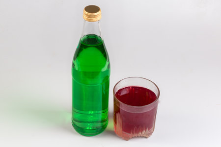 Green non-alcoholic carbonated drink with extract of tarragon addition in closed glass bottle and red cold drink from a boiled fruits in glass on a gray backgroundの写真素材