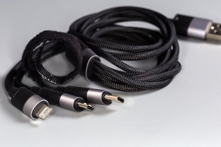 USB-C, micro-USB and Lightning plugs on the edges of coiled black braided slicing cable adapter on a gray background, close-up in selective focusの写真素材