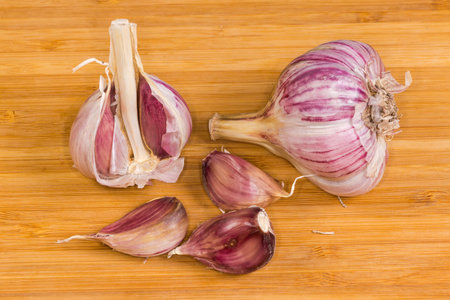 Whole bulb of purple striped garlic, bulb with several removed cloves and several cloves in their husk on a wooden surfaceの写真素材