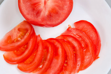 One half and thin slices of the fresh red tomato on dish on a gray background, top view close-up, fragmentの写真素材