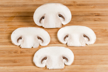 Thin slices of the fresh raw button mushroom cut lengthwise on a wooden cutting board close-upの写真素材