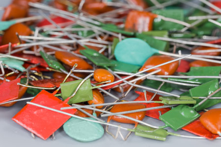 Heap of various ceramic disc and rectangular fixed capacitors and film capacitors with axial and radial connecting leads, fragment close-up in selective focusの写真素材