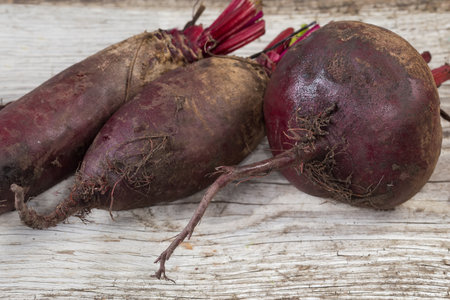 Freshly harvested young red beetroots different shape with roots and part of stems on the old cracked wooden plank, close-up in selective focusの写真素材