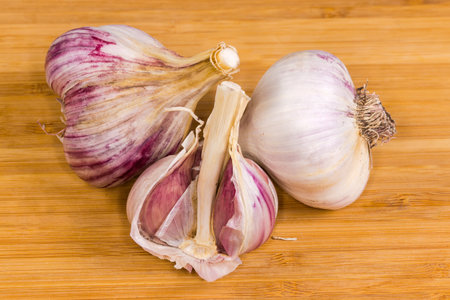 Two whole bulbs of purple striped garlic in their husk and one bulb with several removed cloves on a wooden surfaceの写真素材
