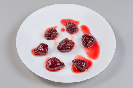 Whole berries of the strawberry jam on the white dish on a gray backgroundの写真素材