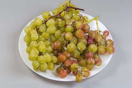 Clusters of the ripe pink and white sultana table grape on a white dish on a gray backgroundの写真素材