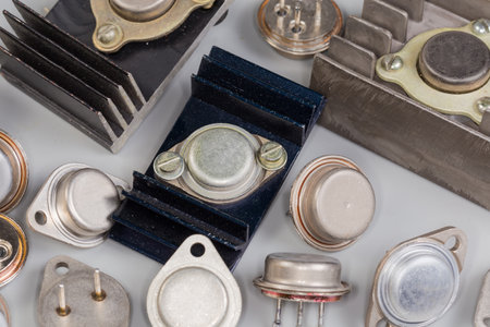 Old bipolar power transistors various purposes in metal packages, some of them installed on finned passive heatsinks on a gray surface, fragment close-upの写真素材